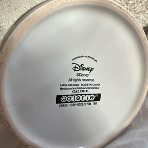 K&ouml;nnte beinhalten: Wei&szlig;e Keramiktasse mit einem Disney-Logo und dem Text "&copy;Disney Alle Rechte vorbehalten. 1-859-538-8500 HERGESTELLT IN CHINA Hergestellt und vertrieben unter Lizenz von GALERIE Galerie 28624 1349-0026/27DN 180"