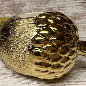 May include: A gold acorn-shaped candle holder with a white candle inside. The holder has a textured surface and a glossy finish.