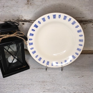 Op de afbeelding: Een wit keramiek dinerbord met een blauw en wit bloemenpatroon rond de rand. Het bord ligt op een wit houten oppervlak.