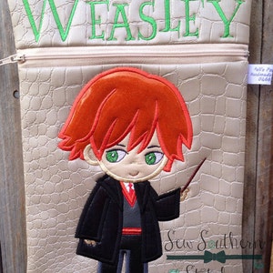 May include: A beige zippered pouch with a red-haired cartoon character holding a wand. The character is wearing a black robe and a red tie. The pouch has the name "WEASLEY" embroidered on the front in green thread. The pouch is made by "Sew Southern Stitches".