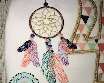 May include: Embroidered design of a dreamcatcher with feathers in pink, purple, teal, and navy blue. The dreamcatcher is hanging from a string. The design is on a white fabric background. The text "NO NUMBER OR NAME INCLUDED" is below the design.