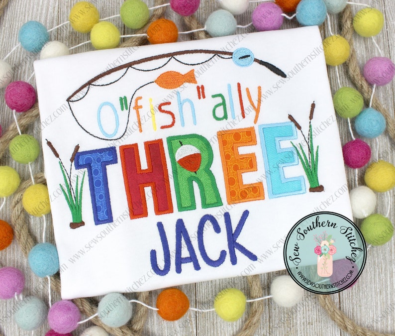May include: A white onesie with colorful embroidered text that reads "O'fish'ally Three Jack". The text is surrounded by a fishing rod, a fish, and reeds.