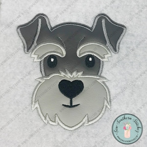 Könnte beinhalten: Ein gestickter Aufnäher mit dem Gesicht eines Zwergschnauzers in Grau- und Weißtönen. Der Hund hat eine herzförmige Nase und schwarze Augen.