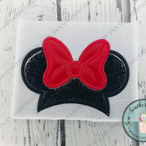 May include: Black and red embroidered mouse ears with a large red bow. The ears are on a white background.