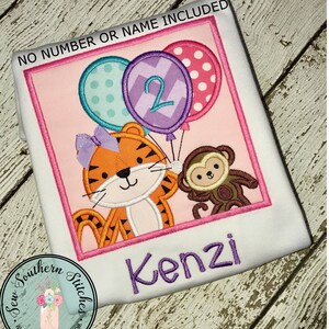 Puede incluir: Una camisa bordada personalizada de color rosa y blanco con un tigre, un mono y globos. La camisa dice "Kenzi" y "No se incluye número ni nombre".