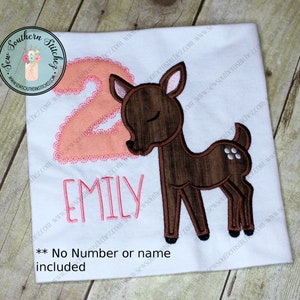 May include: A white t-shirt with a pink number two and a brown deer with closed eyes. The name "Emily" is embroidered below the deer. **No Number or name included**