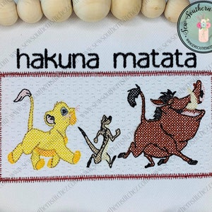 May include: Embroidered patch with the phrase "hakuna matata" in black text. The patch features three cartoon characters: a lion, a meerkat, and a warthog. The characters are embroidered in yellow, brown, and tan thread.