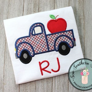 Puede incluir: Una camioneta de reparto azul y roja a cuadros con una manzana roja en la parte trasera. La camioneta tiene una llanta negra y una hoja verde en la manzana. El nombre "RJ" está bordado en rojo debajo de la camioneta.