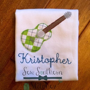 May include: White onesie with a green and white checkered guitar applique and the name "Kristopher" embroidered in blue thread. The text "Sew Southern" is also embroidered in blue thread below the name.
