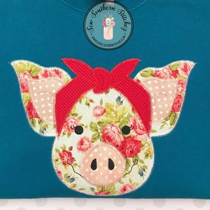 May include: A teal blue sweatshirt with a floral pig applique wearing a red bandana. The pig has pink polka dots on its ears and snout. The text "Sew Southern Stitches" is on the top of the sweatshirt.