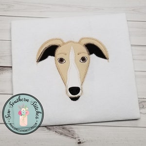 May include: Embroidered design of a light brown and white dog's face with black ears and nose. The design is on a white fabric background.