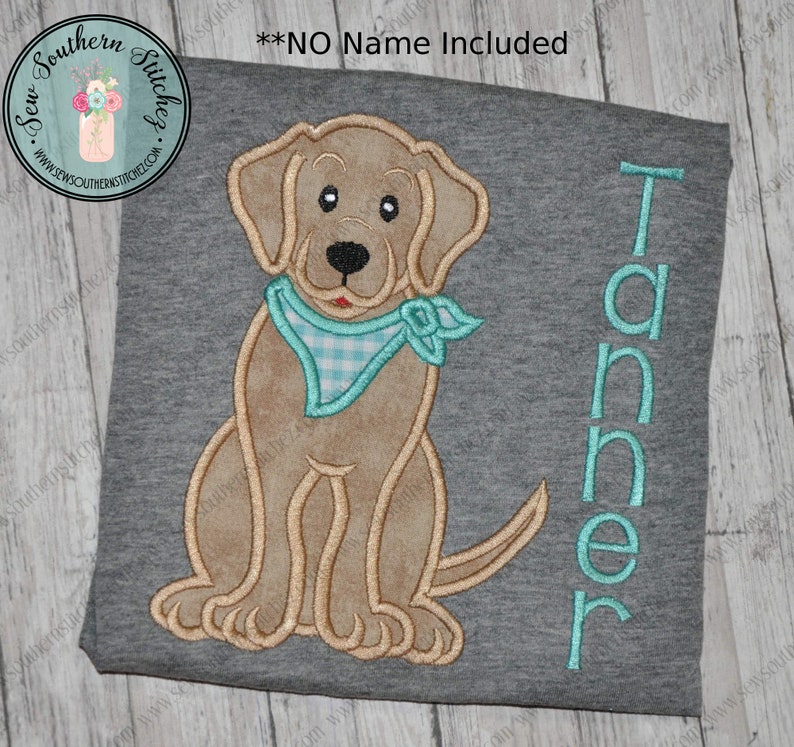 May include: A light gray t-shirt with an embroidered brown dog wearing a blue and white checkered bandana. The name "Tanner" is embroidered in turquoise on the right side of the shirt.