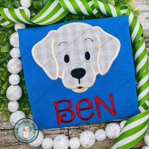Könnte beinhalten: Ein blaues T-Shirt mit einem gestickten Hundekopf in Weiß und Beige mit Karomuster auf der Vorderseite. Der Name "BEN" ist in Rot unter dem Hund gestickt.