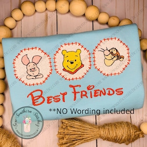 Pode incluir: Uma camiseta azul clara com três imagens bordadas de Winnie the Pooh, Piglet e Tigger. O texto "Best Friends" está bordado em vermelho abaixo das imagens. O texto "**NO Wording included" está impresso em preto abaixo do texto bordado.