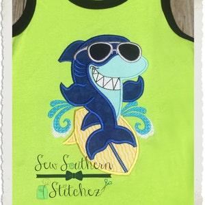 May include: A blue shark wearing sunglasses and riding a yellow surfboard with white waves. The image is on a green background with the text "Sew Southern Stitchez" at the bottom.