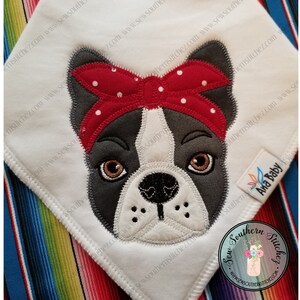 Puede incluir: Diseño bordado de un bulldog francés con un lazo rojo con lunares blancos. El diseño está sobre un fondo de tela blanca. El texto "Sew Southern Stitches" y "Ana Baby" son visibles en la imagen.