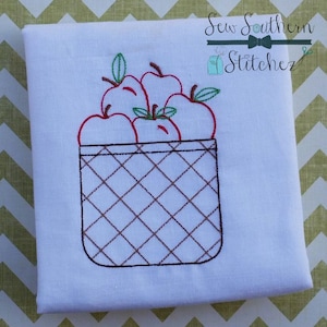 May include: Embroidered design of a basket filled with red apples. The basket is brown and has a checkered pattern. The design is perfect for a fall-themed project.