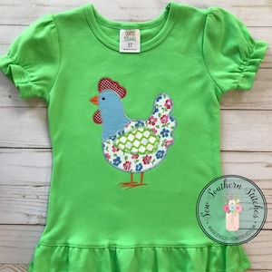 May include: A green short-sleeved shirt with a ruffled hem features a colorful appliqué of a chicken. The shirt has a tag that reads "CBB Blanks 3T Made in China".