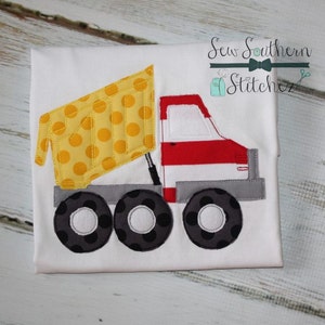 May include: A white t-shirt with a yellow, red, and gray applique of a dump truck. The truck has a yellow bed with black polka dots, a red cab with white stripes, and gray wheels with black polka dots. The text "Sew Southern Stitchez" is in the top right corner of the image.