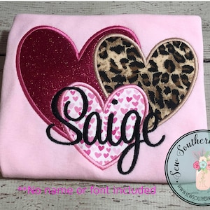 May include: Pink t-shirt with a layered heart design. The hearts are pink, red, and leopard print. The name "Saige" is embroidered in black cursive inside the hearts. "Sew Southern Stitches" is printed in a circle on the bottom right corner of the shirt.