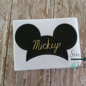 May include: White t-shirt with a black embroidered Mickey Mouse head and the word "Mickey" in gold thread.