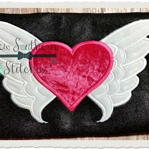 May include: A red heart with white wings embroidered on a black fabric. The heart is made of velvet and the wings are made of a white fabric.