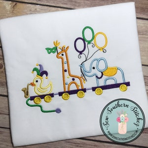 May include: White fabric with an embroidered design of a train carrying a duck, giraffe, and elephant. The duck wears a jester hat and holds a pipe. The giraffe has a mask and the elephant has balloons. The train is purple.