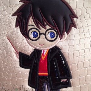 Puede incluir: Parche bordado de un personaje de dibujos animados de Harry Potter con una túnica negra, un suéter rojo y gafas. El personaje sostiene una varita mágica en su mano derecha.