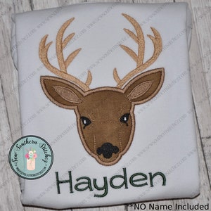 May include: Embroidered design of a brown deer head with antlers on a white background. The name Hayden is embroidered in green below the deer.