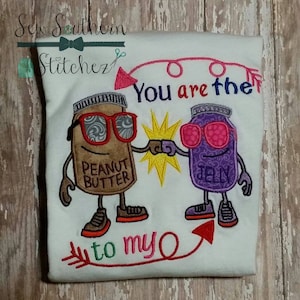 Puede incluir: Camiseta blanca bordada con un diseño de tarro de mantequilla de cacahuete y mermelada. Los tarros llevan gafas de sol y tienen brazos y piernas. El texto dice "You are the to my O".