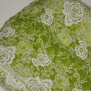 Könnte beinhalten: Grüner Stoff mit weißem, gesticktem Blumenmuster. Der Stoff hat eine weiche, samtige Textur.