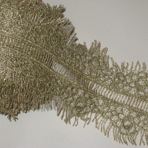 May include: Gold glitter lace trim with a fringed edge. The lace has a delicate pattern and is perfect for adding a touch of sparkle to any project.