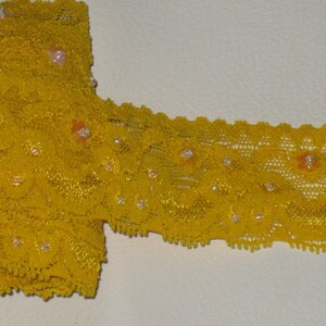May include: Yellow lace trim with small white beads and orange flower accents.