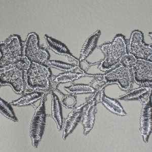 May include: Silver lace trim with a floral design. The lace features delicate flowers and leaves.