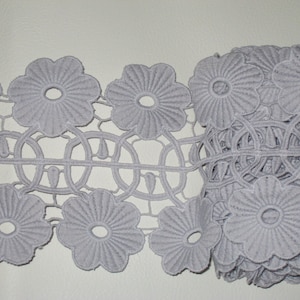 May include: Grey lace trim featuring a floral design. The lace has a delicate, intricate pattern with small flowers and circles.