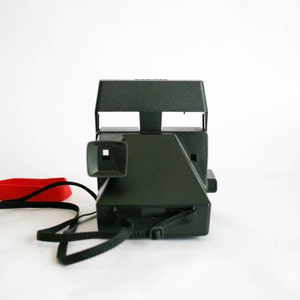 May include: A black Polaroid camera with a red strap. The camera has a viewfinder and a flash.