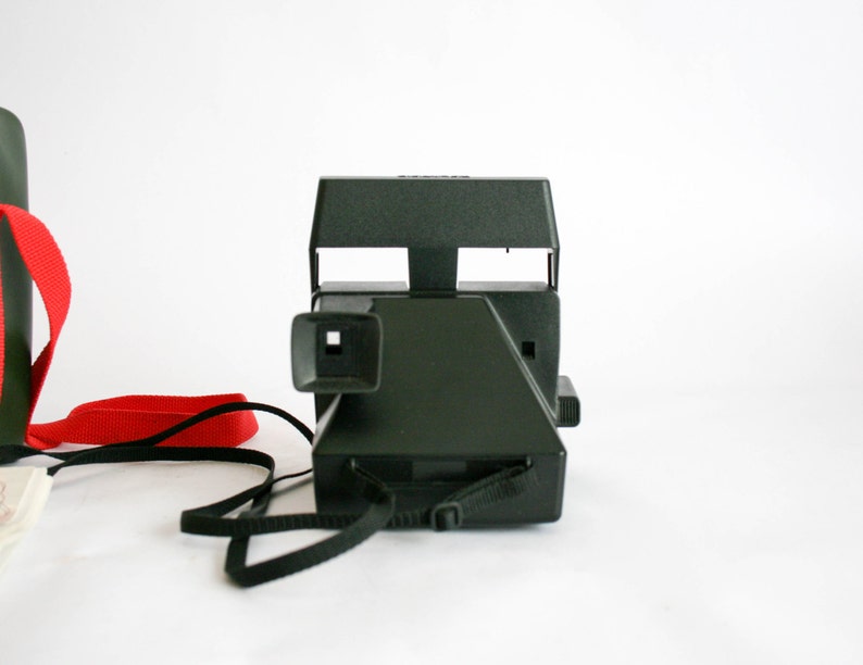 May include: A black Polaroid camera with a red strap. The camera has a viewfinder and a flash.