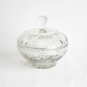 Può includere: Una zucchieriera di vetro trasparente con coperchio. La zucchieriera ha un design in vetro tagliato e una base rotonda.