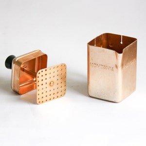 K&ouml;nnte beinhalten: Eine Kaffeemaschine aus Kupfer mit einem herausnehmbaren Filter und einem schwarzen Griff. Die Kaffeemaschine ist mit "MONTANIA" beschriftet.