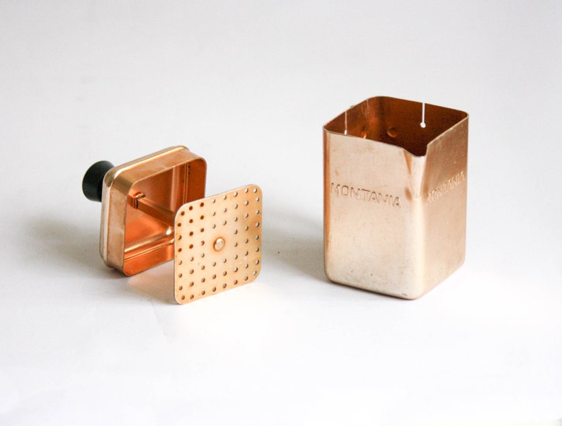 K&ouml;nnte beinhalten: Eine Kaffeemaschine aus Kupfer mit einem herausnehmbaren Filter und einem schwarzen Griff. Die Kaffeemaschine ist mit "MONTANIA" beschriftet.