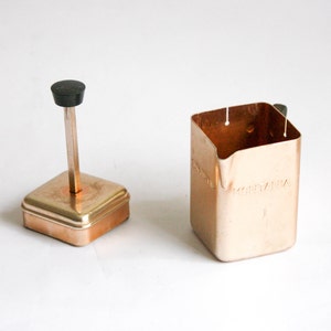 K&ouml;nnte beinhalten: Ein Milchaufsch&auml;umer aus Kupfer mit einem schwarzen Knopf oben und dem Wort "MONTANA" auf der Seite.