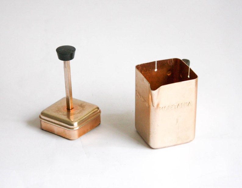 K&ouml;nnte beinhalten: Ein Milchaufsch&auml;umer aus Kupfer mit einem schwarzen Knopf oben und dem Wort "MONTANA" auf der Seite.