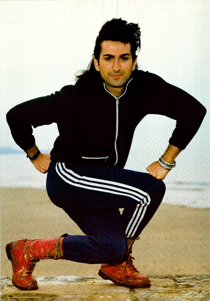 Puede incluir: Una persona con una chaqueta negra con cremallera, pantalones de ch&aacute;ndal azul marino con rayas blancas y botas rojas. La persona est&aacute; arrodillada sobre una superficie clara, con los brazos doblados y las manos en las caderas.