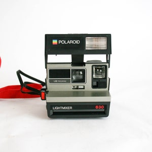 May include: A black and silver Polaroid Land Camera with a red button and the words "LIGHTMIXER" and "630" printed on the front. The camera has a built-in flash and a viewfinder.