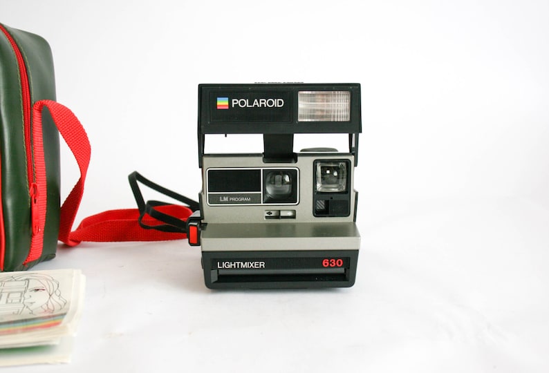 May include: A black and silver Polaroid Land Camera with a red button and the words "LIGHTMIXER" and "630" printed on the front. The camera has a built-in flash and a viewfinder.