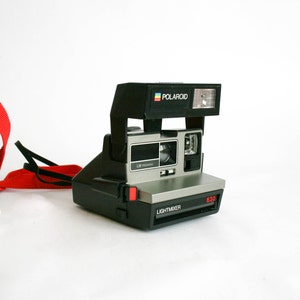 May include: A black and silver Polaroid Land Camera with a red button and the text "LIGHTMIXER" and "630" on the front. The camera has a built-in flash and a green and red carrying case.