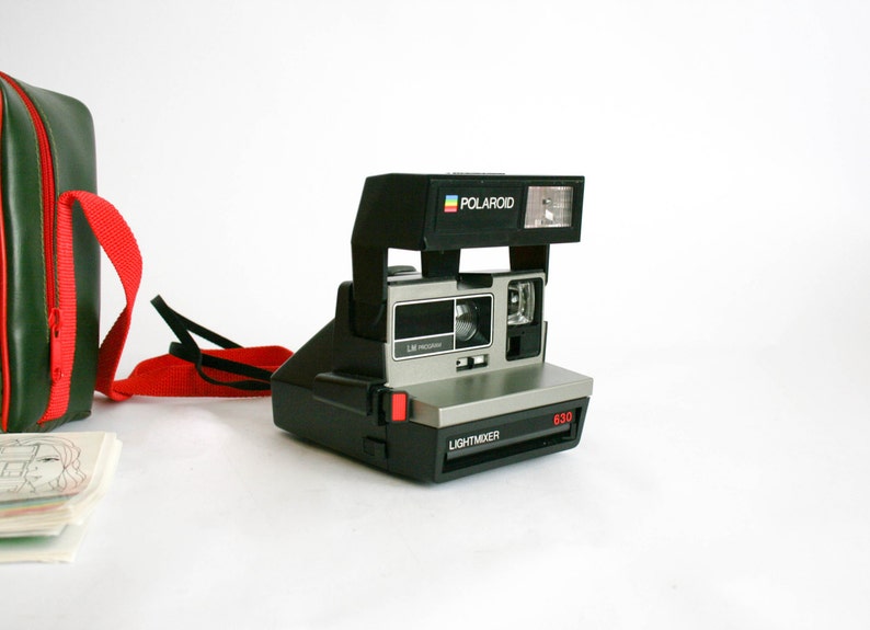 May include: A black and silver Polaroid Land Camera with a red button and the text "LIGHTMIXER" and "630" on the front. The camera has a built-in flash and a green and red carrying case.