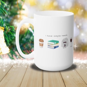 May include: White ceramic mug with the text "I have simple needs" and illustrations of a cup of coffee, a stack of books, a white poodle, and a glass of red wine.