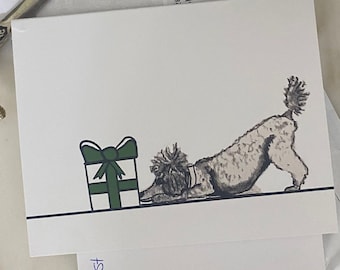May include: A white greeting card featuring a black and white sketch of a poodle in a play bow position next to a white gift box with a dark green ribbon and bow. The illustration is set against a plain white background with a thin black line.