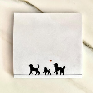 May include: A white notepad with a black line at the bottom and three black silhouettes of poodles. A small orange butterfly is above the poodles.